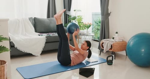 Asia woman in sportswear watching fitness online video on tablet with fitness ball.