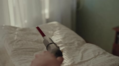 Firstperson View of Man Steaming Fresh White Blanket on Bed in Bright Bedroom Using Steam Cleaner