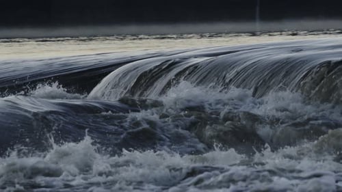 Close-up of a dark, textured wave cresting with white foam against a blurred background
