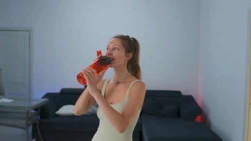 Woman Drinks Water From Bottle After Workout Indoors