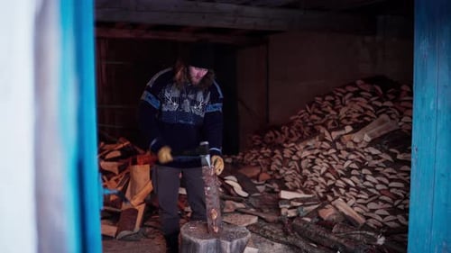 Man Chopping Wood With Axe In A Barn With Pile Of Firewood. static shot