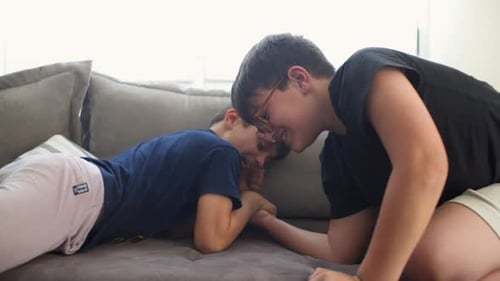 Two caucasian kids having fun at home, playing armwrestling game. Medium shot, side view 4K