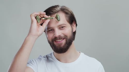 Smiling man uses jade roller on his forehead