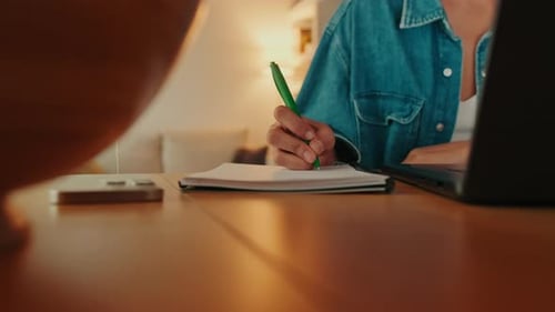 Woman Writing in Notebook at Desk With Laptop