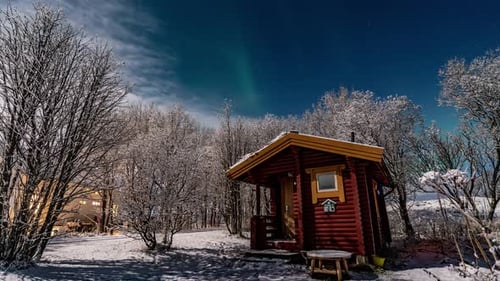 time lapse of a small wooden cabin in winter forest under the northern lights in norway
