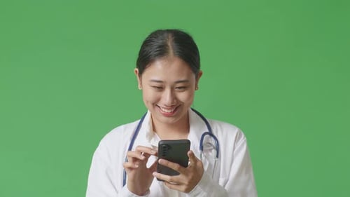 Close Up Of Asian Woman Doctor With Stethoscope Using Smartphone While Standing On Green Screen