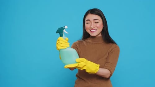 Smiling Asian Maid Wearing Protective Gloves While Showing Chemical Detergent Spray in Front of
