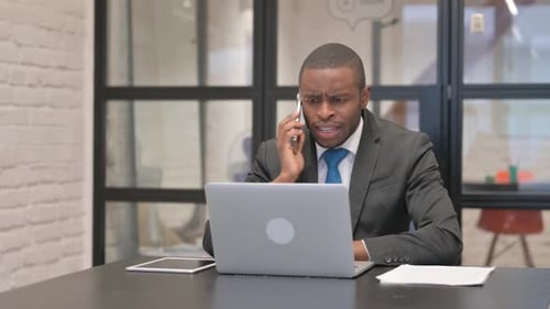 Angry African Businessman Talking on Phone in Office