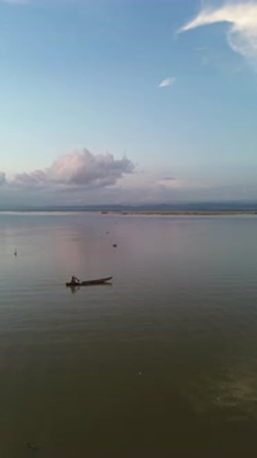 Vertical drone footage of a fisherman on his boat in the lake