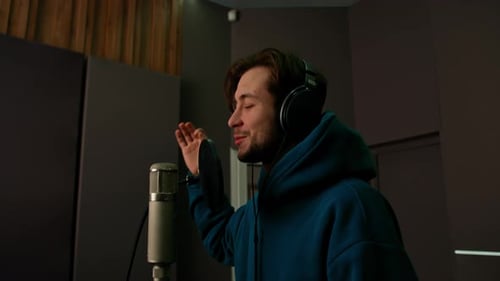 Rap singer with headphones and microphone emotionally recording new song in professional studio