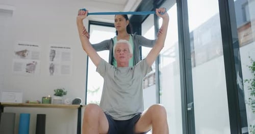 Senior Man Exercising With Resistance Band Assisted by Trainer