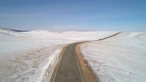 Aerial View on a Road Between the White Snowy Hills with Cars Driving on It Against the Blue Sky