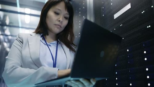 Close-up of Female Asian IT Engineer Working on a Laptop in Data Center full of Rack Servers.