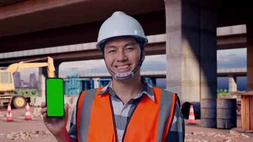 Close Up Of Asian Male Engineer Smiling And Showing Green Screen Smartphone At Building Site