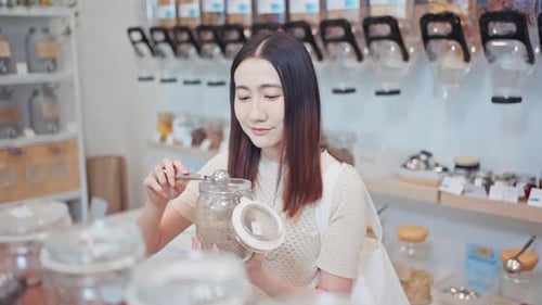 Young woman filling a glass jar with cereal in a zero waste store