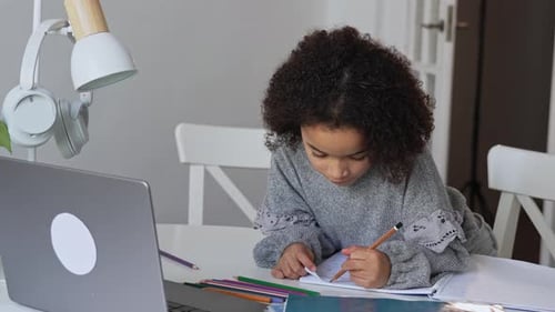 Primary School African American Student Child with Headphones Hand Writing in Book Using Laptop