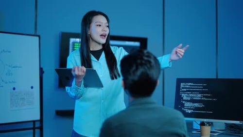 Female IT manager holding a tablet discusses software development and coding with a male programmer