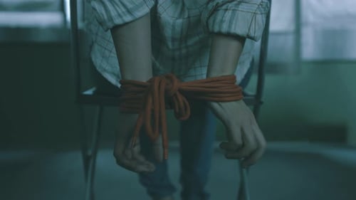 kidnapped young woman tied is sitting on chair. Hands tied with a rope. She's trying to free herself