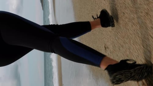 Female legs in sneakers running on beach with waves, close up. Vertical video