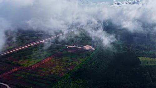 Aerial view of wind turbine tower in green fields covered by thick fog