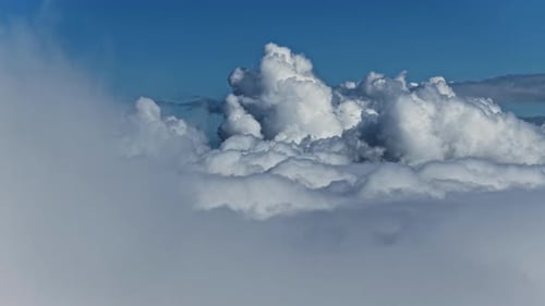 Towering cumulus clouds seen above the cloud layer against clear blue sky, aerial view