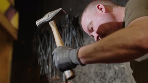 Focused blacksmith in workshop strikes red hot metal on anvil with hammer, slomo