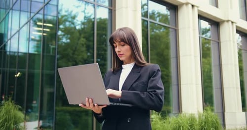 Businesswoman Works on Laptop Outside Modern Office Building