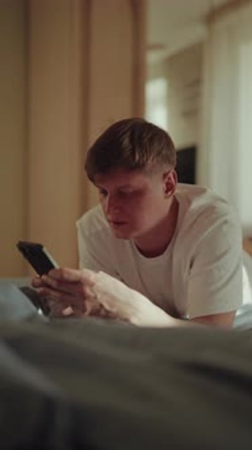 Young Man Using Smartphone in Bedroom