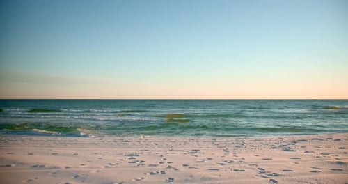 Shots of the ocean on a warm, sunny evening with footprints in the sand