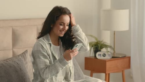 Smiling Woman Using Phone Sitting on Bed