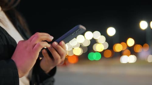 Person Using Phone at Night With Bokeh Lights