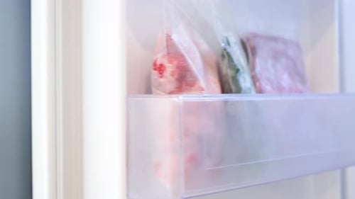 Frozen vegetables in plastic bags in freezer close-up, side view.