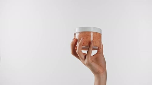 Hand Holding Peach Body Scrub Jar on White