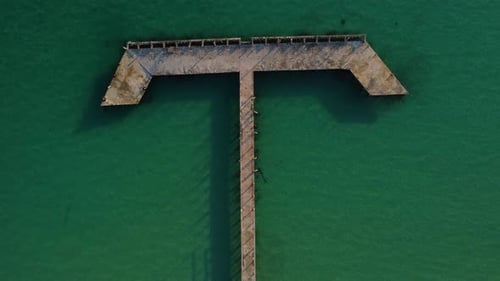Pier wood dock over green turquoise ocean water on island, aerial top down view