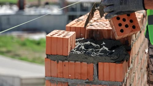 CloseUp of Mason Laying Hollow Bricks with Mortar Precision Brickwork on Urban Construction Site