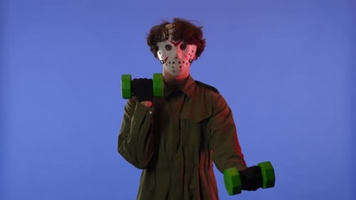 Man in White Mask Swinging His Arms with Green Dumbbells on Blue Background with Red Neon Light