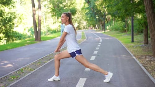 Fit Woman Runner Stretching Legs on Asphalt Road in Park