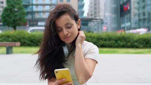Pretty Woman Sitting on Steps Outdoor While Using Smartphone and Looking at Screen