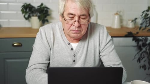 Adult Man Uses Laptop at Kitchen Table
