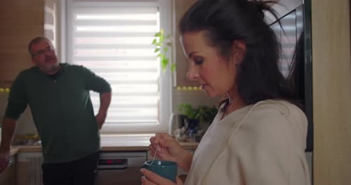 Woman Stirring Coffee in Kitchen with Man Nearby