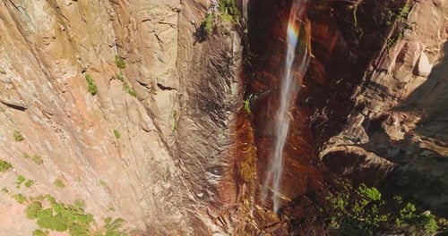 Rainbow appearing in the stream falling from huge cliff. Drone footage raising along the steep rocks