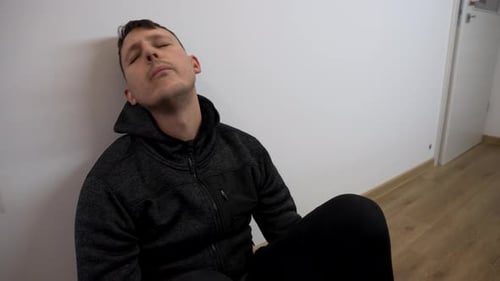 Man Sitting Against Wall Looking Upset in an Interior