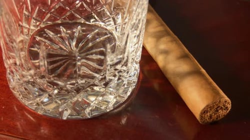 Close up of empty crystal glass and cigar coming out of shadow.
Whiskey is poured into glass.