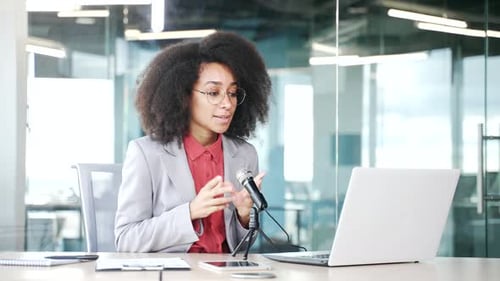 Young african american businesswoman with a microphone is recording a podcast using a laptop sitting