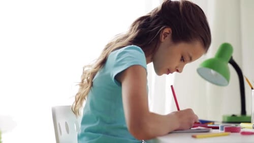 Girl Writes in Notebook at Desk Indoors