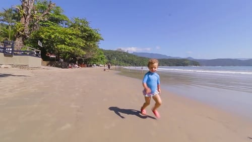 camera orbiting around 4 year old happy young cute girl running freely on the beach with mountains b