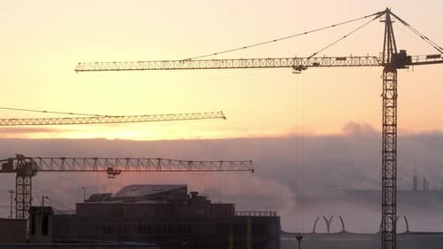 Cranes at a construction site lift loads against the background of a city