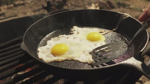 Close up cooker using spatula to separate two eggs cooking in the frying pan