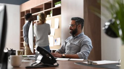 Lächelnder Geschäftsmann mit Brille, der im Büro am Desktop-Computer arbeitet.
Mitte