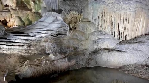 Giant limestone underground cave with pure white stalactites and stalagmites. Pan view from the pond